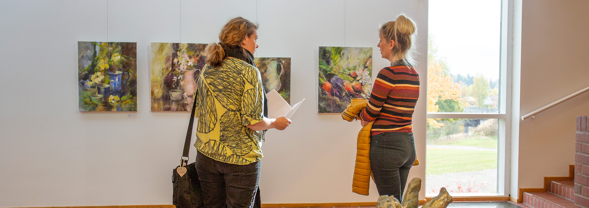 Kaksi ihmistä katselemassa värikkäitä taideteoksia Kuusankoskitalon galleriassa.