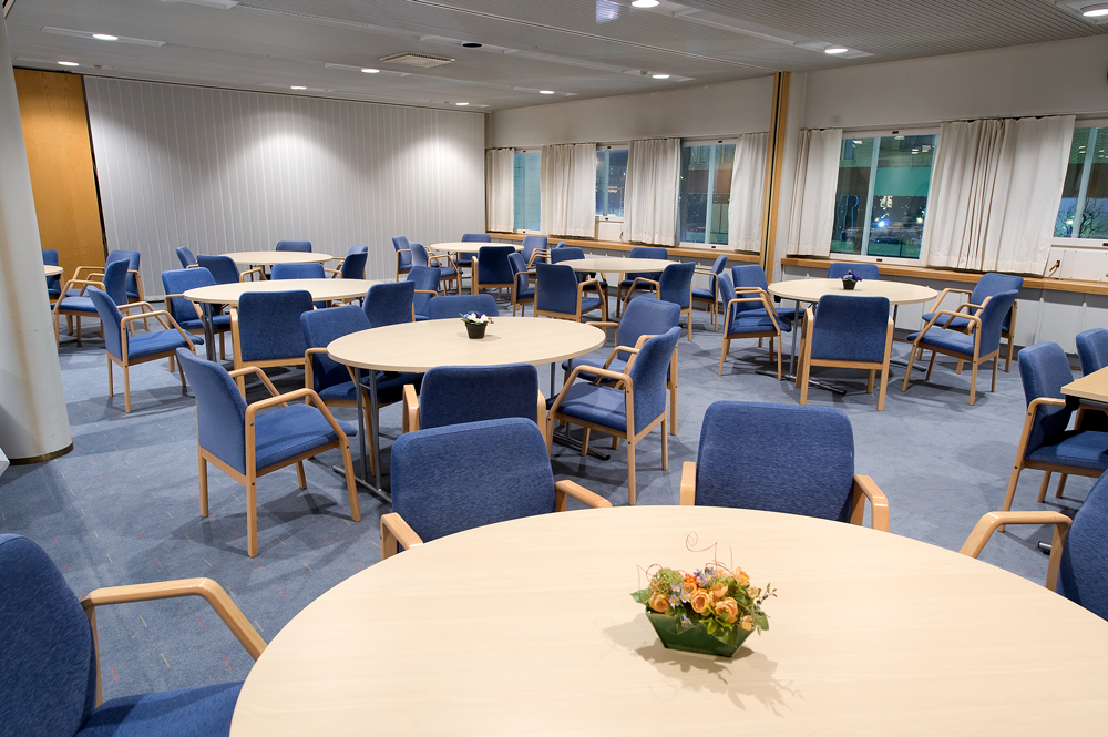 Kuusankoskitalon Hirvelä-kokoustila, pyöreät pöydät, sinisellä kankaalla päällystetyt tuolit