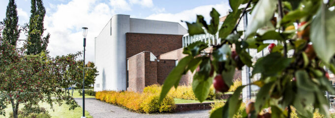 Kuusankoskitalo kuvattuna rantapuiston puolelta, etualalla kirsikkapuita.