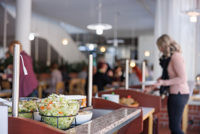 Kuusankoskitalon Cafen salaattibuffet etualalla, taustalle vierailja ottamassa ruokaa lautaselle.